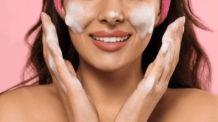 Leende kvinna med löddrande ansiktsrengöring på huden. Fräsch och effektiv hudvårdsrutin för en ren och strålande hy.