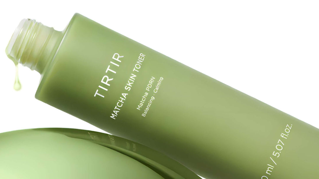En flaska av Safe Me Relief Essence Toner ligger lutad mot en bomullsrondell på en pastellgrön bakgrund, belysningen skapar en mjuk skugga.