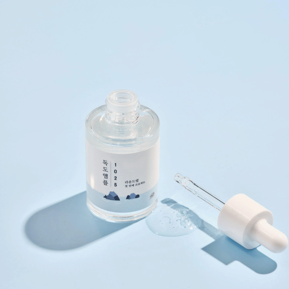 Otwarta butelka 1025 Dokdo Ampoule z pipetą obok, na niebieskim tle tworzącym miękki cień.