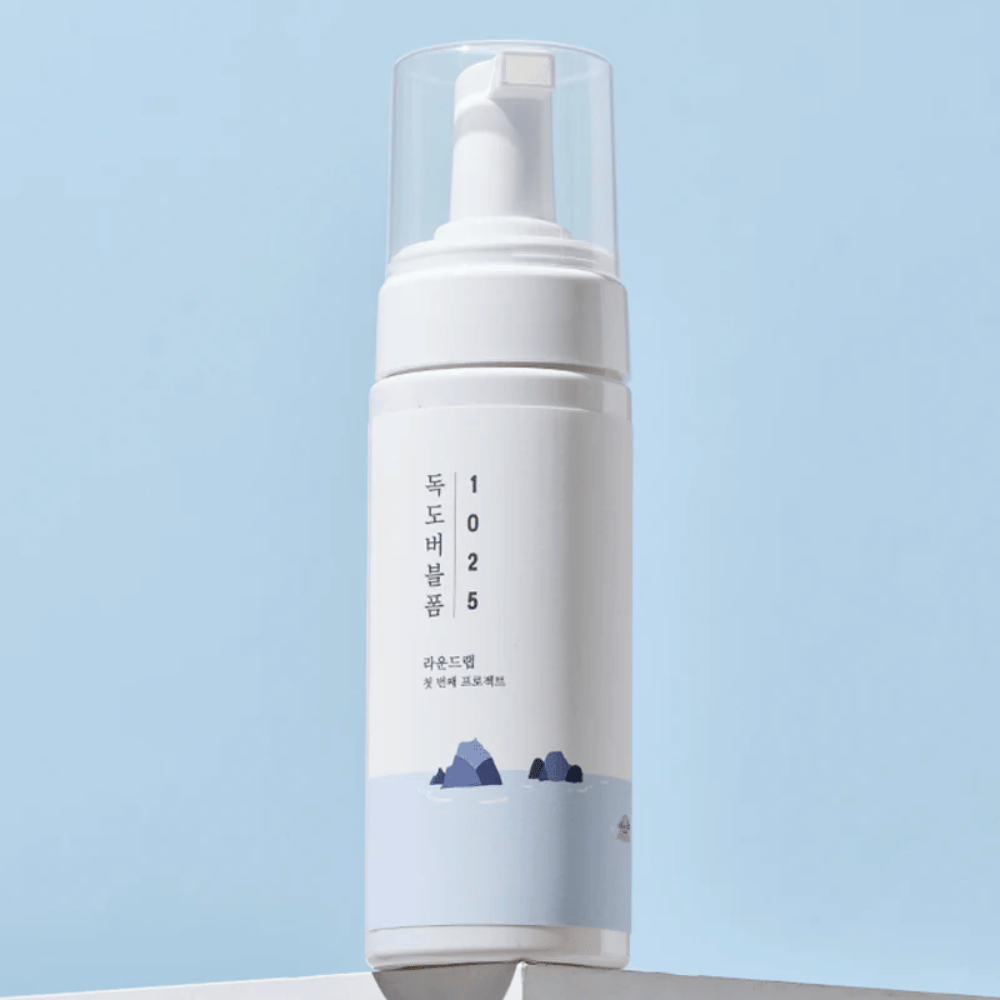  Produkt jest "1025 Dokdo Bubble Foam" od ROUND LAB, zapakowanym w białą butelkę z pompką o minimalistycznym designie. Jest przeznaczony do głębokiego oczyszczania twarzy bez podrażnień.