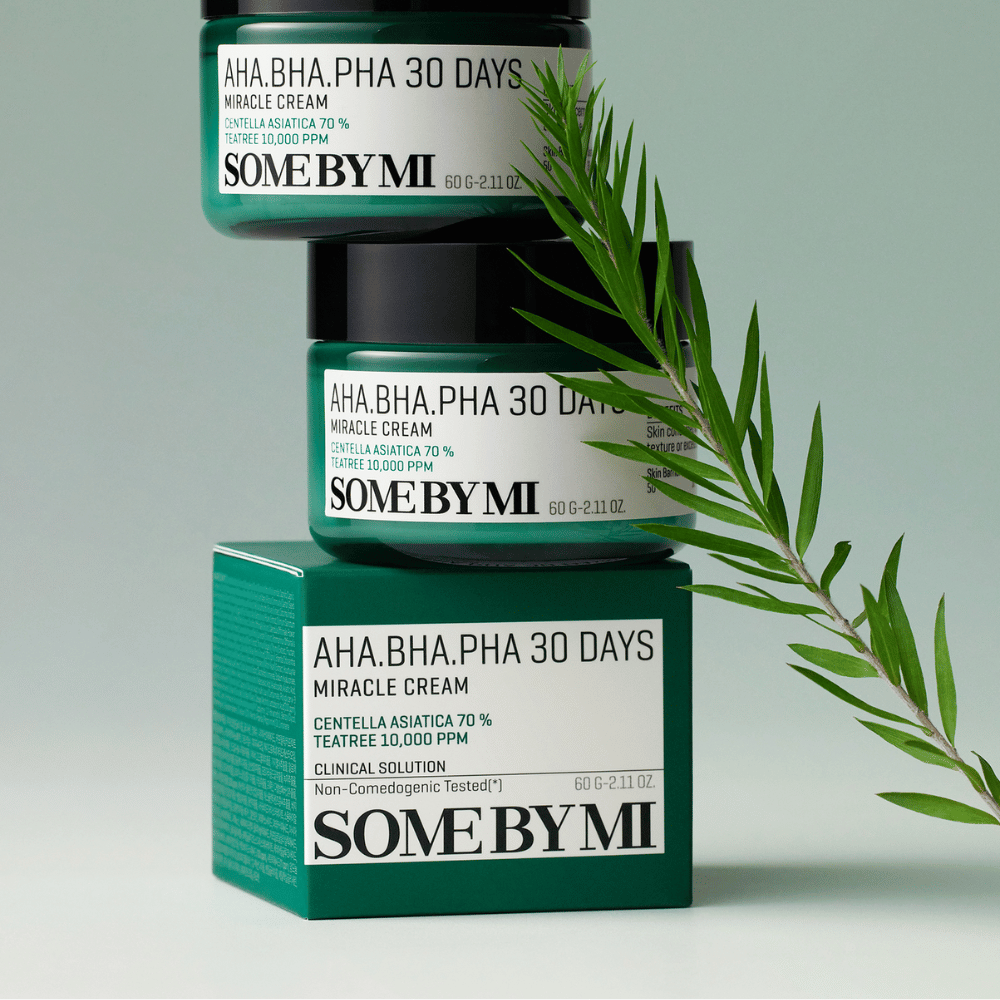 Zdjęcie przedstawiające dwa słoiki "SOME BY MI AHA, BHA, PHA 30 Days Miracle Cream" ustawione na zielonkawej kratce. Krem, który jest bogaty w centella asiatica i olej tea tree, jest zaprojektowany, aby poprawić jakość skóry i łagodzić problemy skórne. Działa nawilżająco i łagodząco.
