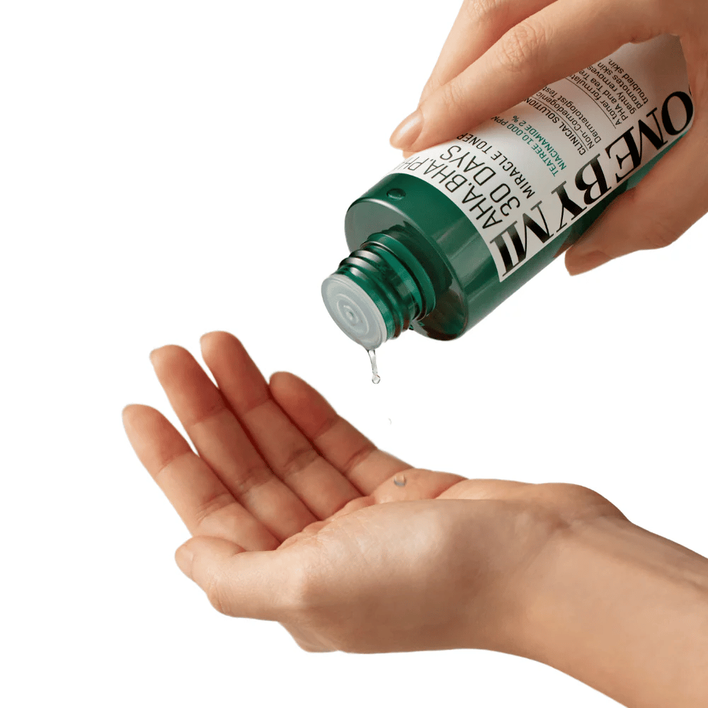 Ręka trzyma zieloną butelkę z napisem "AHA, BHA, PHA 30 Days Miracle Toner" i wyciska przezroczysty płyn na dłoń drugiej ręki, gotowy do użycia.