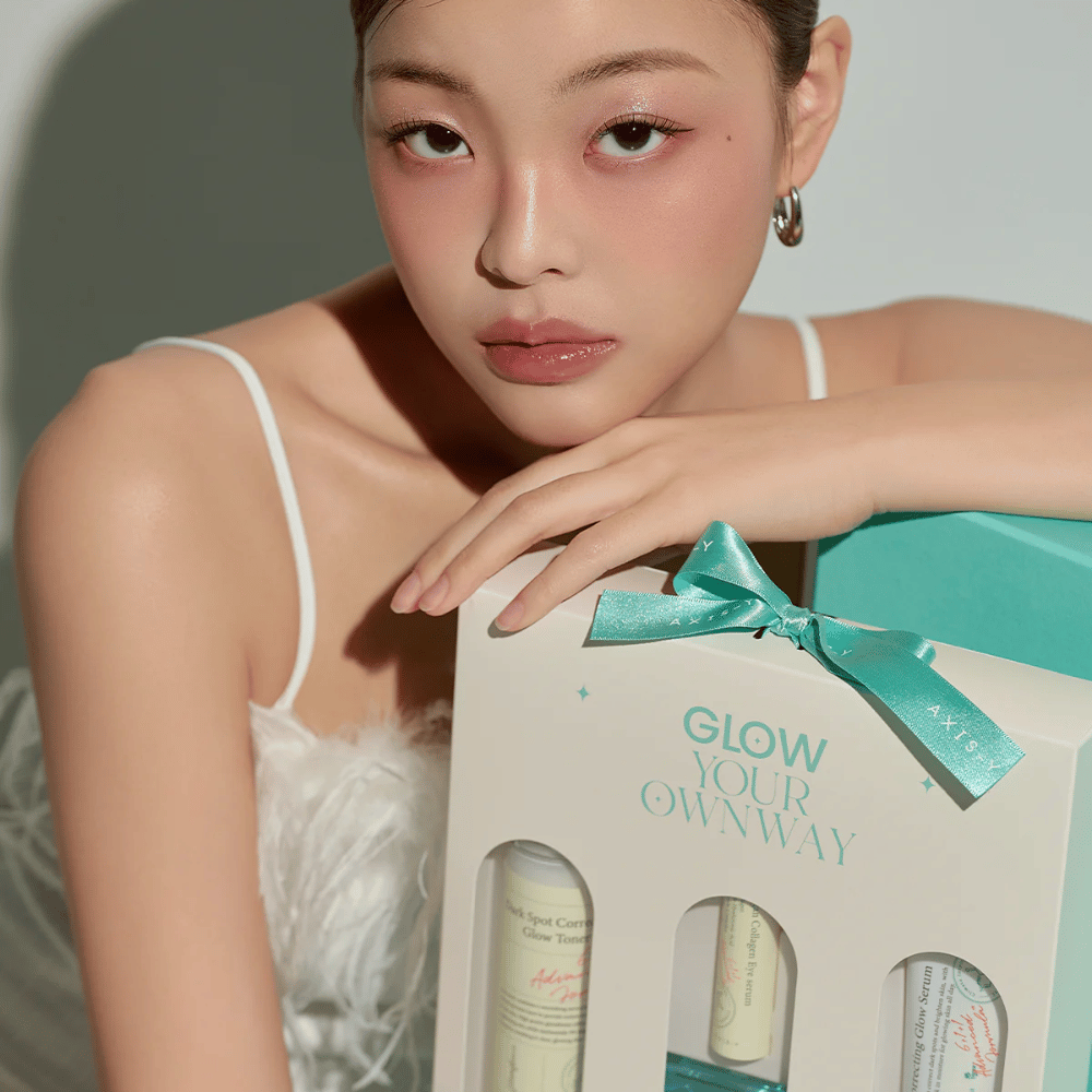 Modelka z eleganckim makijażem trzyma w rękach “Glow Your Own Way”-pudełko prezentowe od AXIS-Y:s – stylowe Zestaw do pielęgnacji skóry idealne jako prezent dla siebie lub kogoś, kogo lubisz.