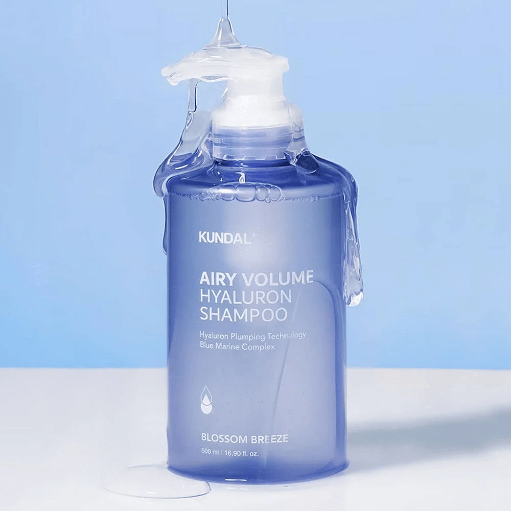KUNDAL Airy Volume Hyaluron Shampoo Blossom Breeze w niebieskiej butelce z pompką, z kwasem hialuronowym i kompleksem Blue Marine, sfotografowany z płynącą wodą.