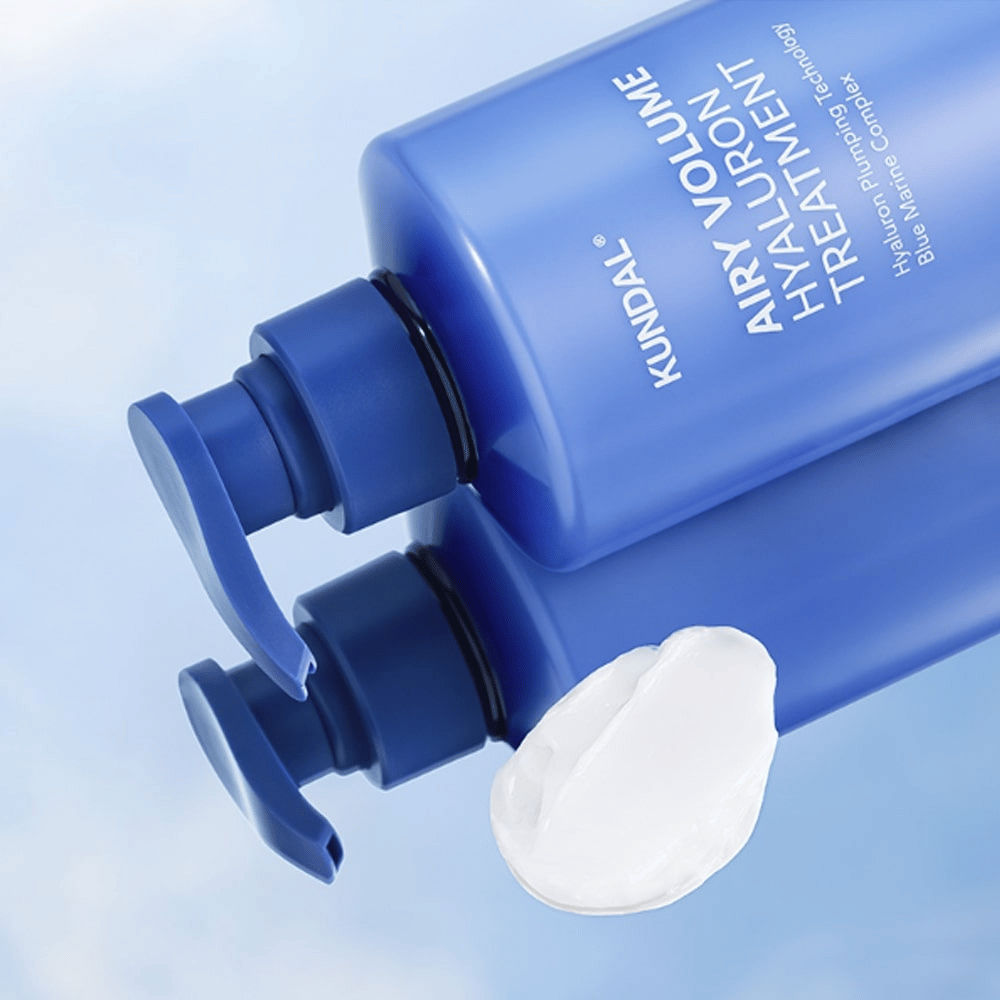 KUNDAL Airy Volume Hyaluron Treatment w niebieskiej leżącej butelce z pompką, z widocznym białym produktem kremowym obok.