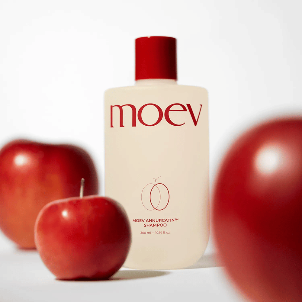 MOEV Annurcatin Shampoo umieszczony wśród czerwonych jabłek – inspirowany antyoksydantami jabłka Annurca, które zapewniają mocniejsze, zdrowsze i bardziej lśniące włosy.