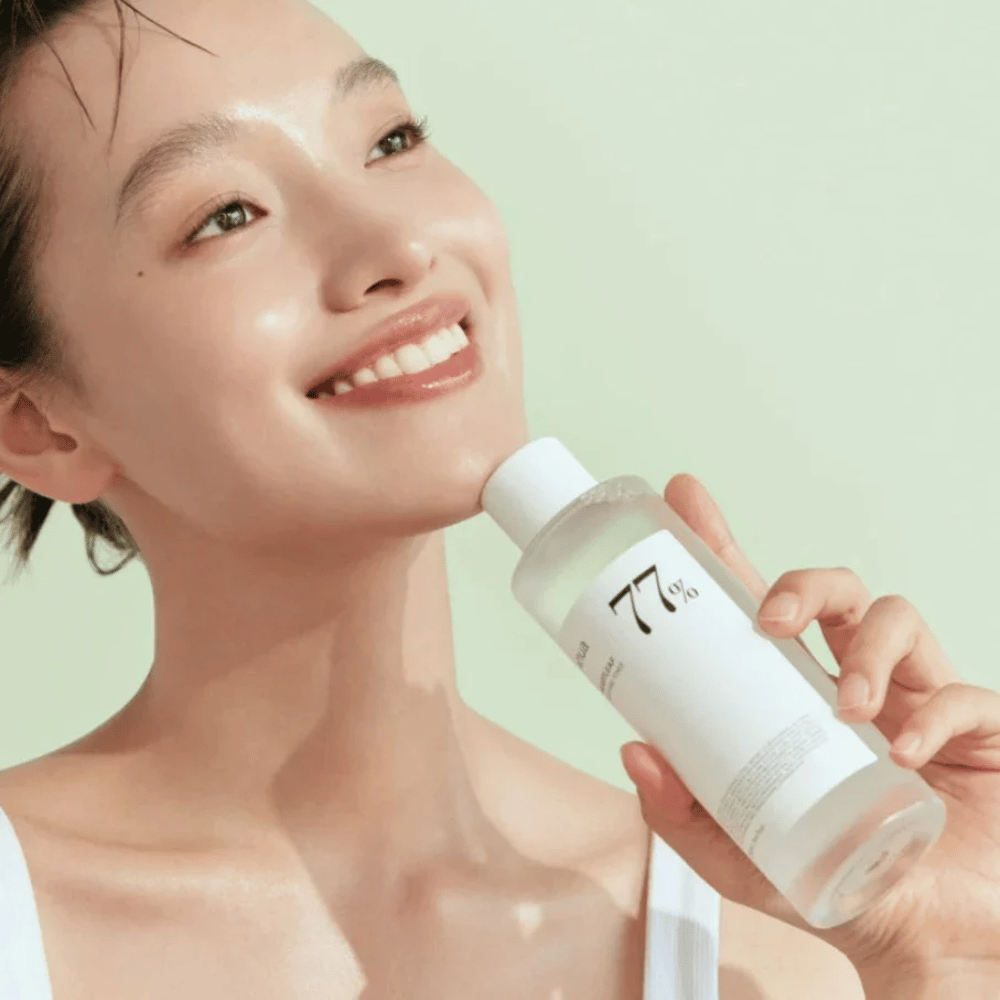 Kobieta łagodzi swoją wrażliwą skórę butelką Heartleaf 77% Soothing Toner od Anua, zawierającą ekstrakt z liści kameleona.