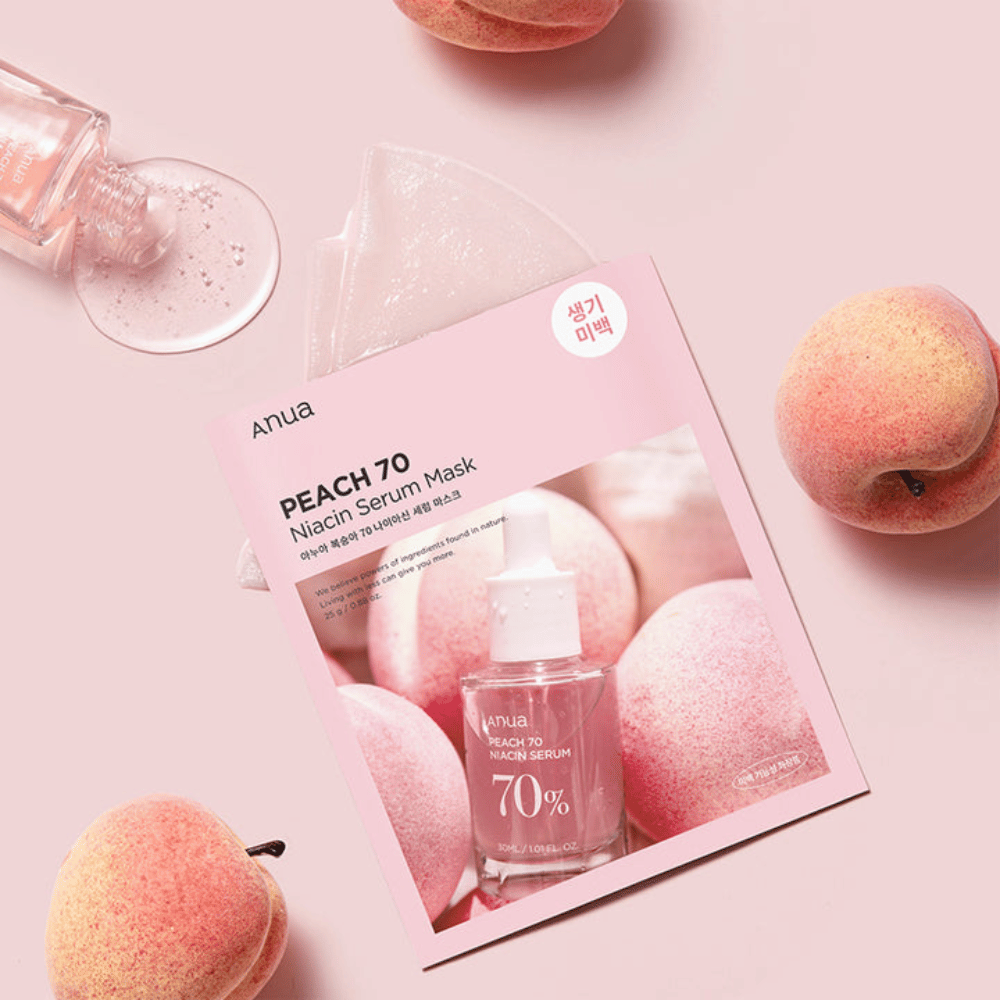 Zdjęcie Anua PEACH 70 Niacin Serum Mask, otoczone brzoskwiniami i butelką z serum. Zdjęcie ma miękkie różowe tło, które uzupełnia różowe opakowanie i podkreśla produkt oraz składniki.