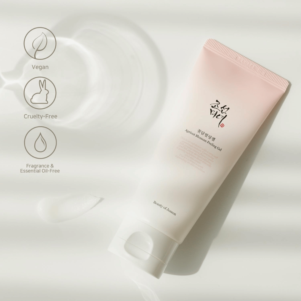 Tubka z Apricot Blossom Peeling Gel leży na odbijającej powierzchni z ikonami wskazującymi, że produkt jest wegański, przyjazny dla zwierząt i wolny od zapachów i olejków eterycznych.