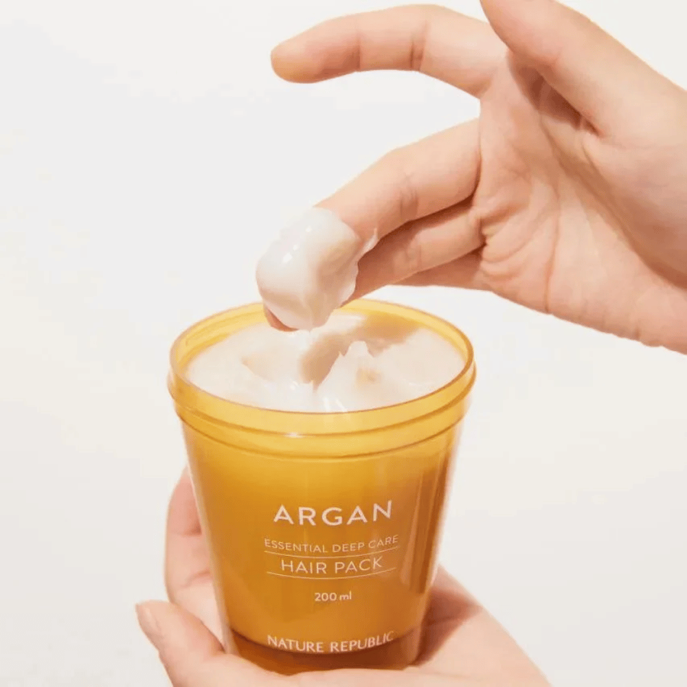 Ręka nabiera kremową formułę z Nature Republic Argan Essential Moisture Repairing Hair Mask – intensywne odżywienie dla suchych włosów.