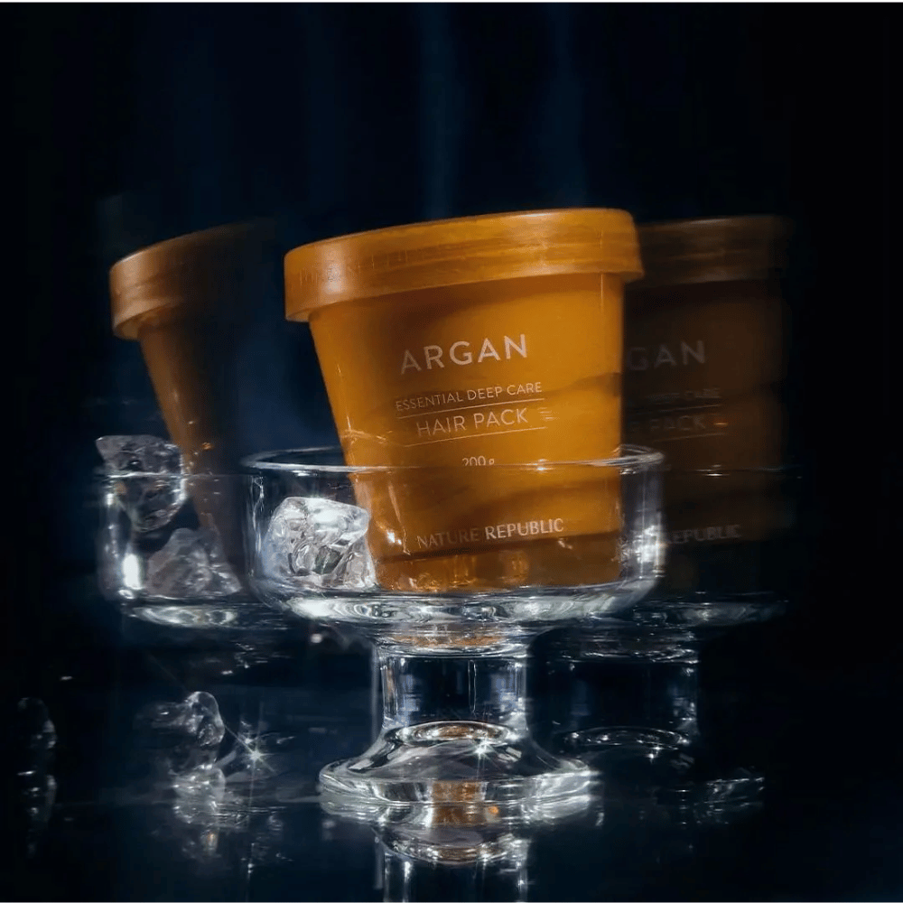 Nature Republic Argan Essential Moisture Repairing Hair Mask umieszczona na szklanym talerzu z kostkami lodu – luksusowa i pielęgnacyjna maska do włosów.
