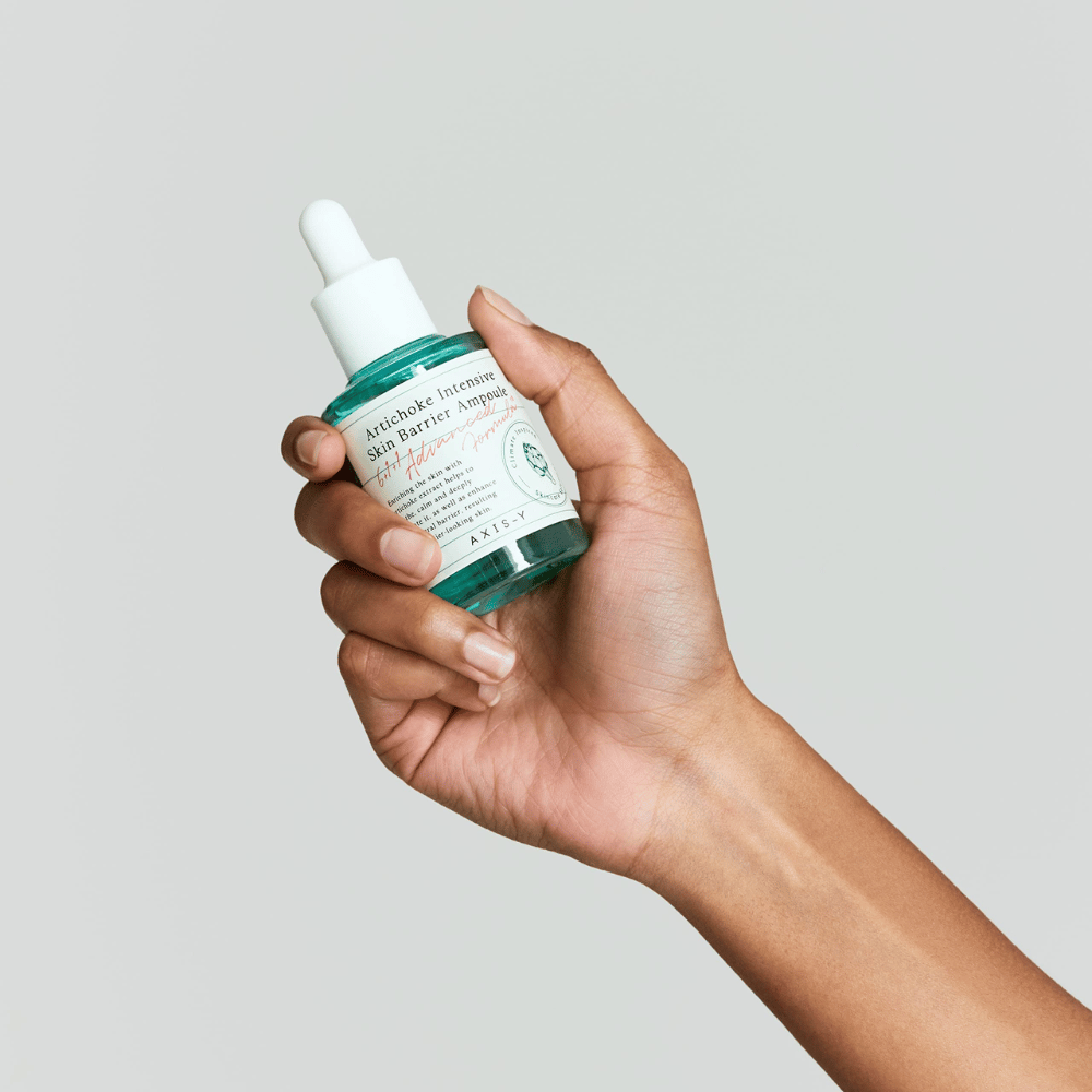 Ręka trzyma butelkę serum do pielęgnacji skóry z etykietą "Artichoke Intensive Skin Barrier Ampoule.