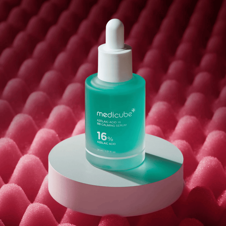 Zdjęcie produktu Medicube Azelaic Acid 16 BB Calming Serum umieszczonego na białym podium z różowym teksturowanym tłem, które podkreśla kojący i poprawiający kondycję skóry profil serum.