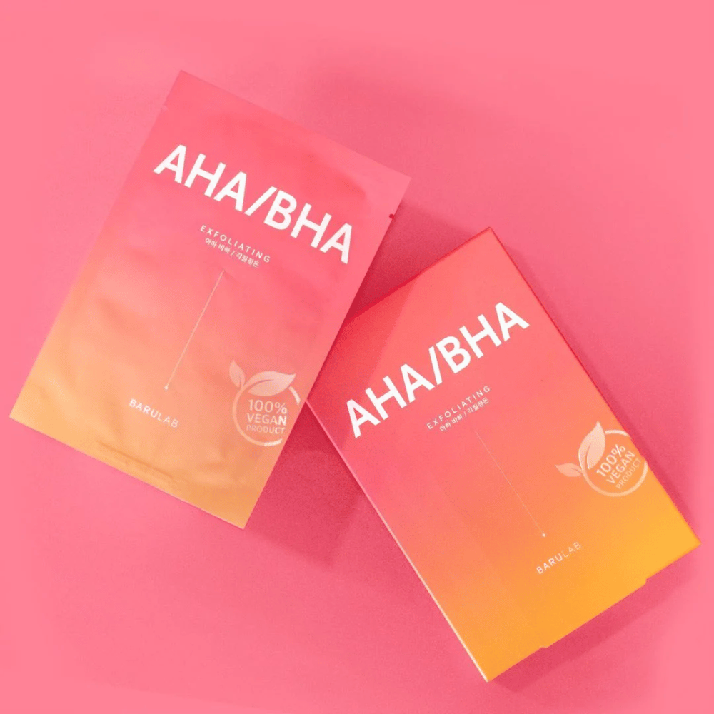 Dwa produkty od BARULAB, jeden w torbie i jeden w kartonie, oba oznaczone jako "AHA/BHA" i "Exfoliating" na różowym tle. Produkty są oznaczone jako "100% Produkt wegański".