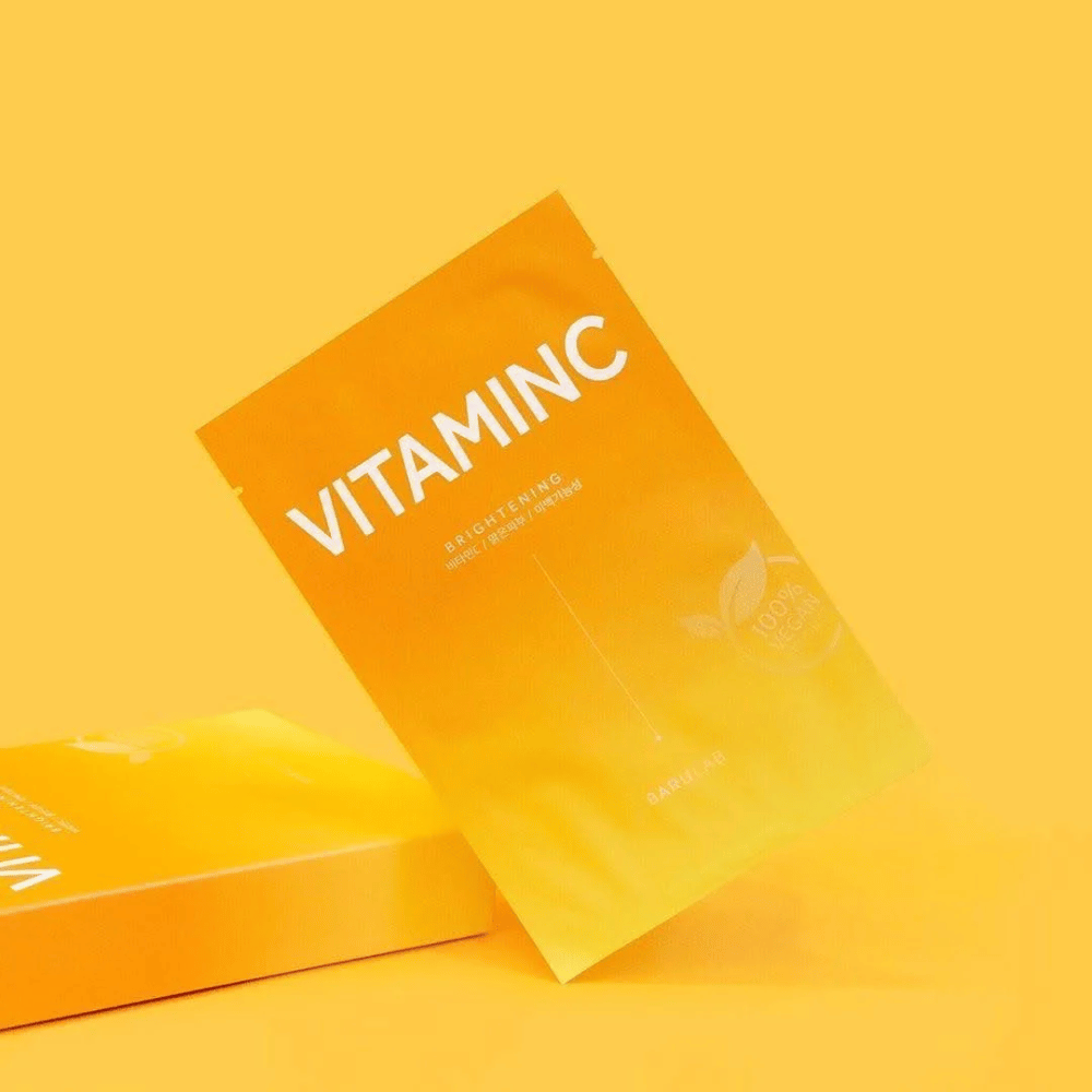 Stos opakowań masek BARULAB "VITAMINC Brightening", wszystkie oznaczone jako "100% Vegan Product". Opakowania mają kolor w różnych odcieniach pomarańczowego i żółtego, ustawione na jednolitym żółtym tle.
