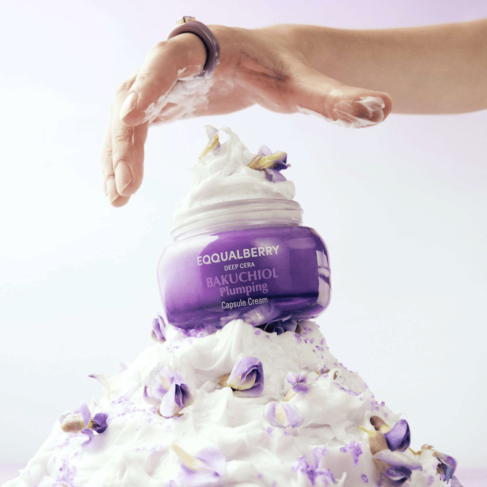 EQQUALBERRY Bakuchiol Plumping Capsule Cream umieszczony na stosie ubitego kremu z płatkami kwiatów – symbolizuje nawilżenie i pielęgnację.