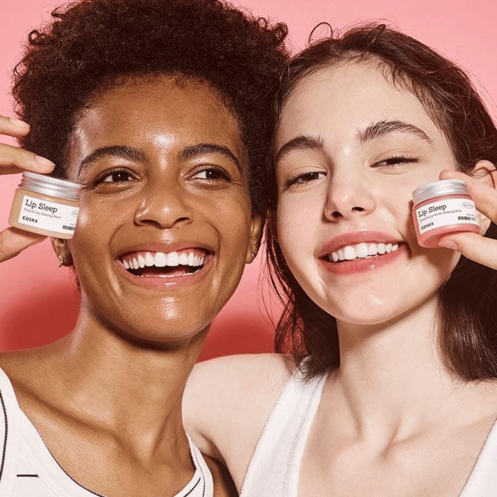 Dwie osoby uśmiechają się i trzymają słoiczki COSRX Lip Sleep. Obrazek przekazuje miękkie, nawilżone usta i naturalny efekt rozświetlenia produktu.