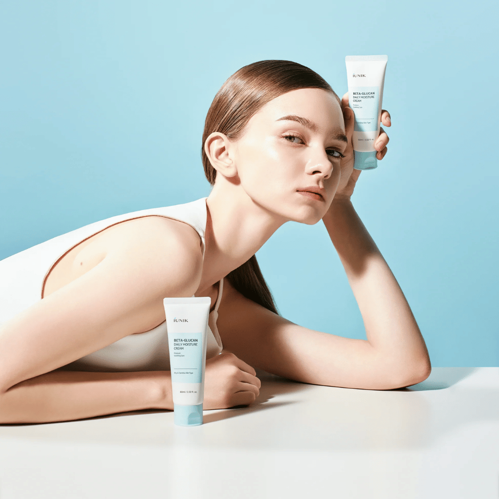 Zdjęcie lifestylowe, na którym modelka pozuje z iUNIK Beta-Glucan Daily Moisture Cream na jasnoniebieskim tle. Obraz przekazuje czyste, świeże i nawilżające odczucie, jednocześnie wyraźnie eksponując produkt.