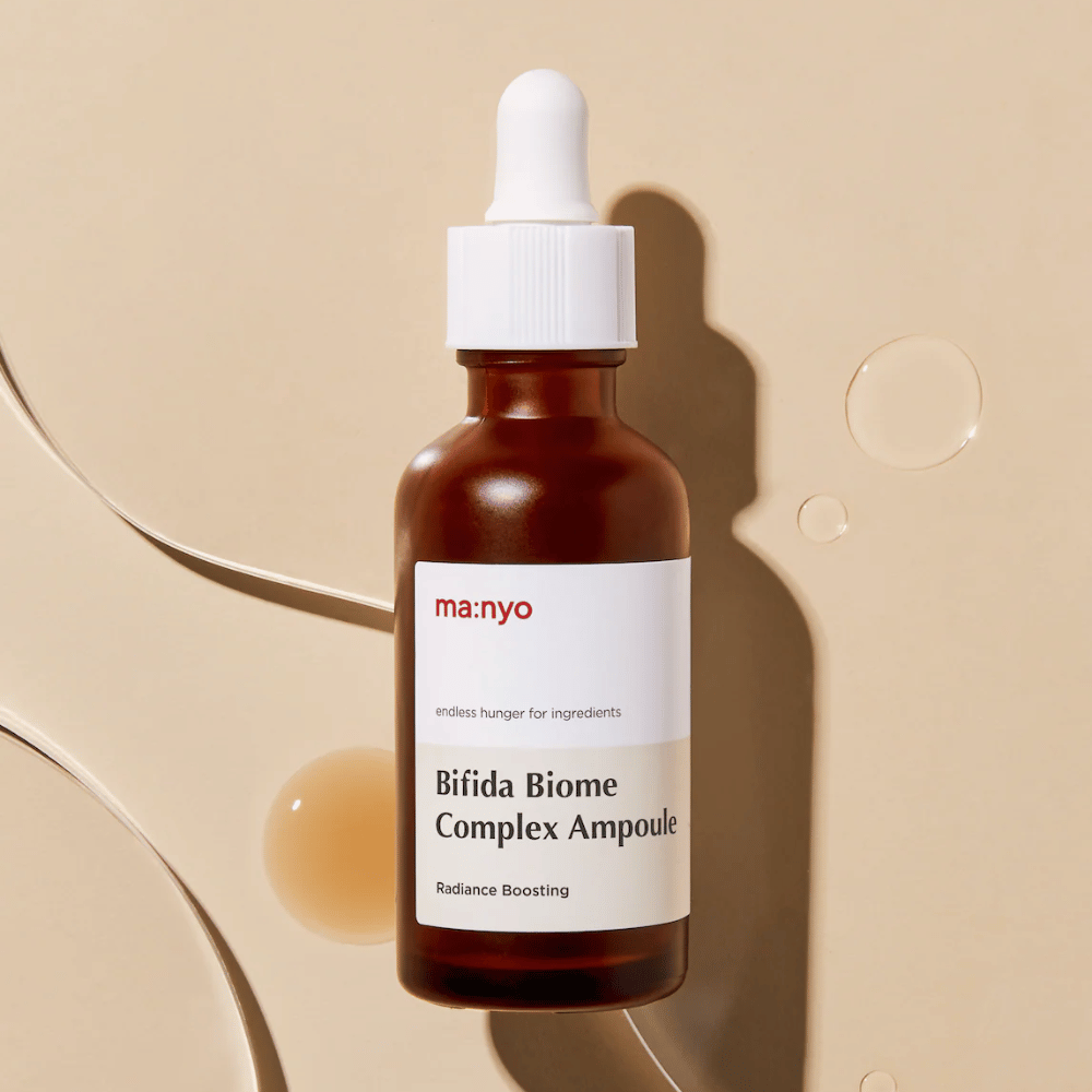 Stylowe zdjęcie produktu ma:nyo Bifida Biome Complex Ampoule z naciskiem na design butelki i krople serum w tle.