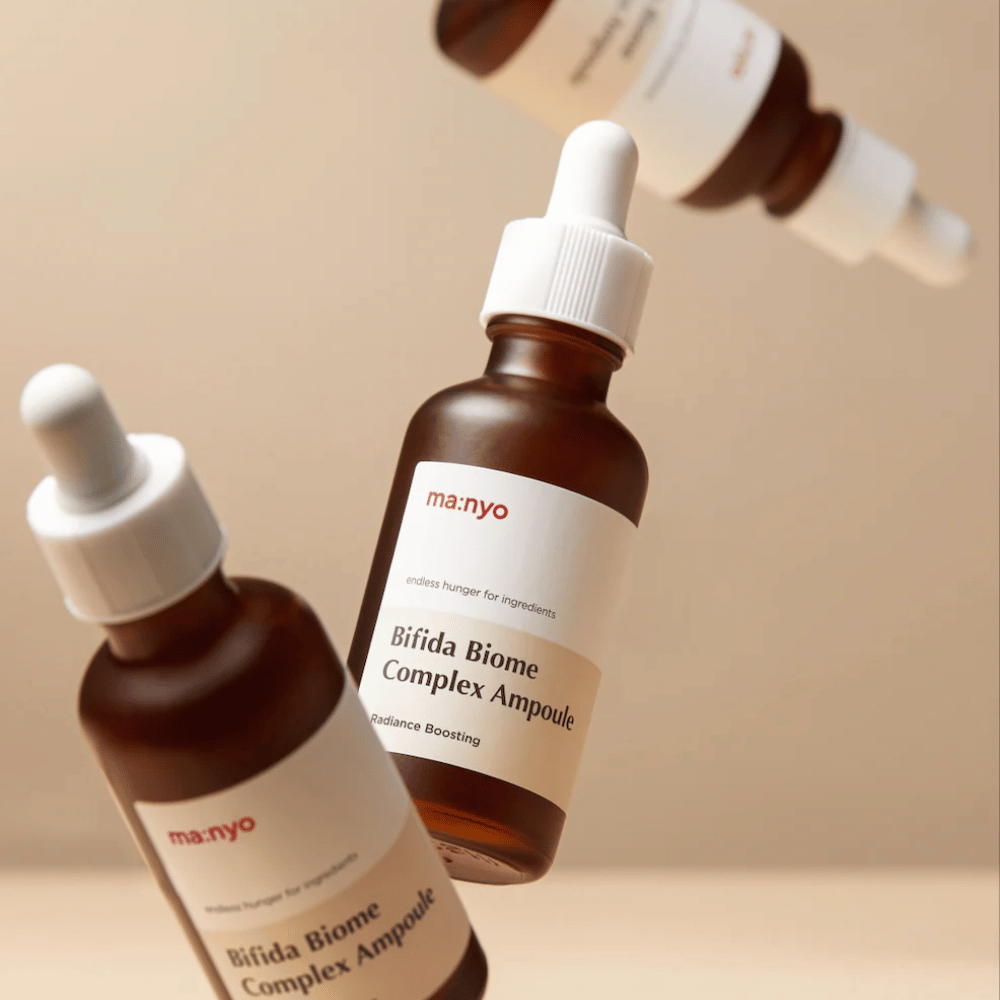 Zdjęcie produktu z kilkoma unoszącymi się butelkami ma:nyo Bifida Biome Complex Ampoule na beżowym tle, nadającym nowoczesny i minimalistyczny charakter.