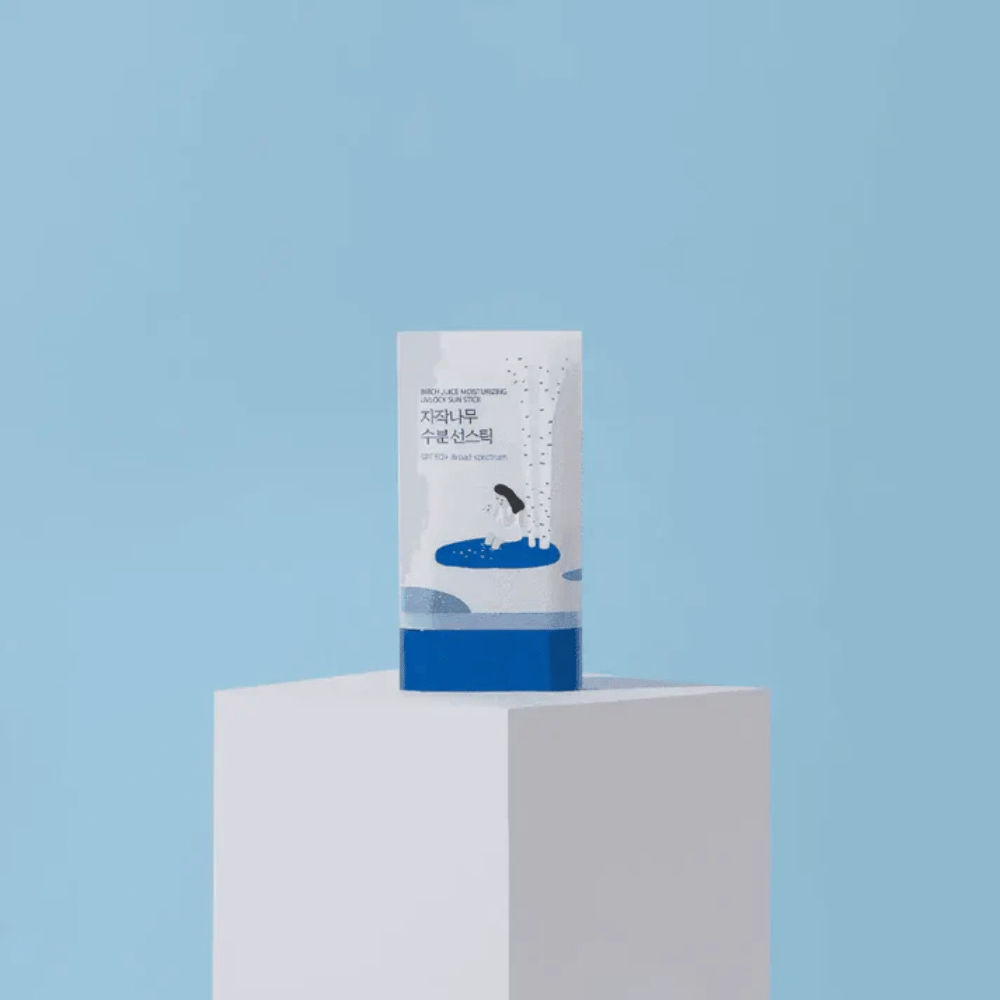 ROUND LAB Birch Juice Moisturizing Sun Stick SPF50+ stoi na postumencie na niebieskim tle – nawilżająca ochrona przeciwsłoneczna w sztyfcie