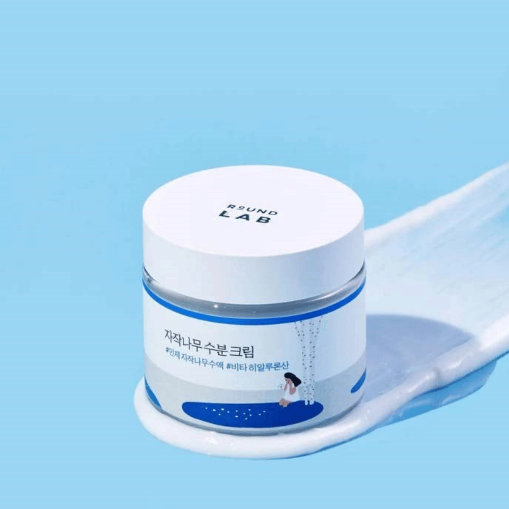 Round Lab Birch Juice Moisturizing Cream w niebieskawym słoiku z białą pokrywką, stojącym w warstwie kremu na niebieskim tle.