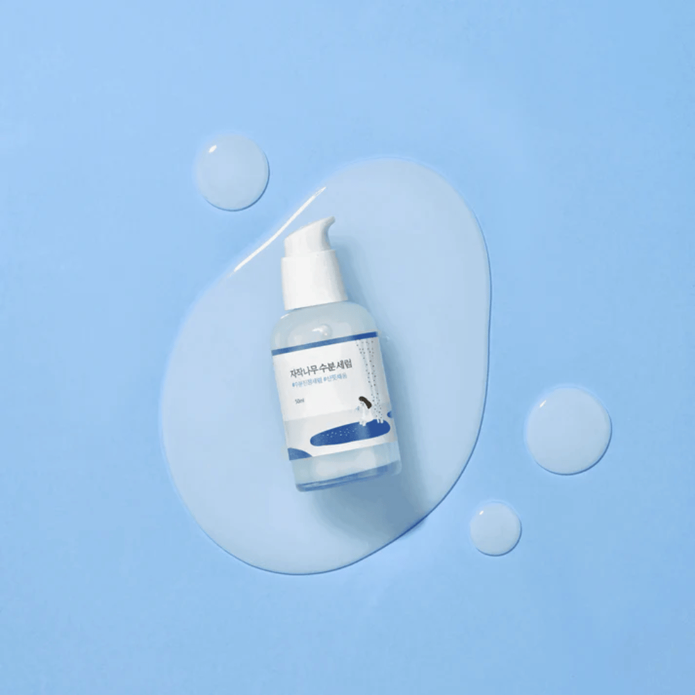 Round Lab Birch Juice Moisturizing Serum w przezroczystej butelce z pompką umieszczonej na niebieskim tle z kroplami i rozlanym serum.