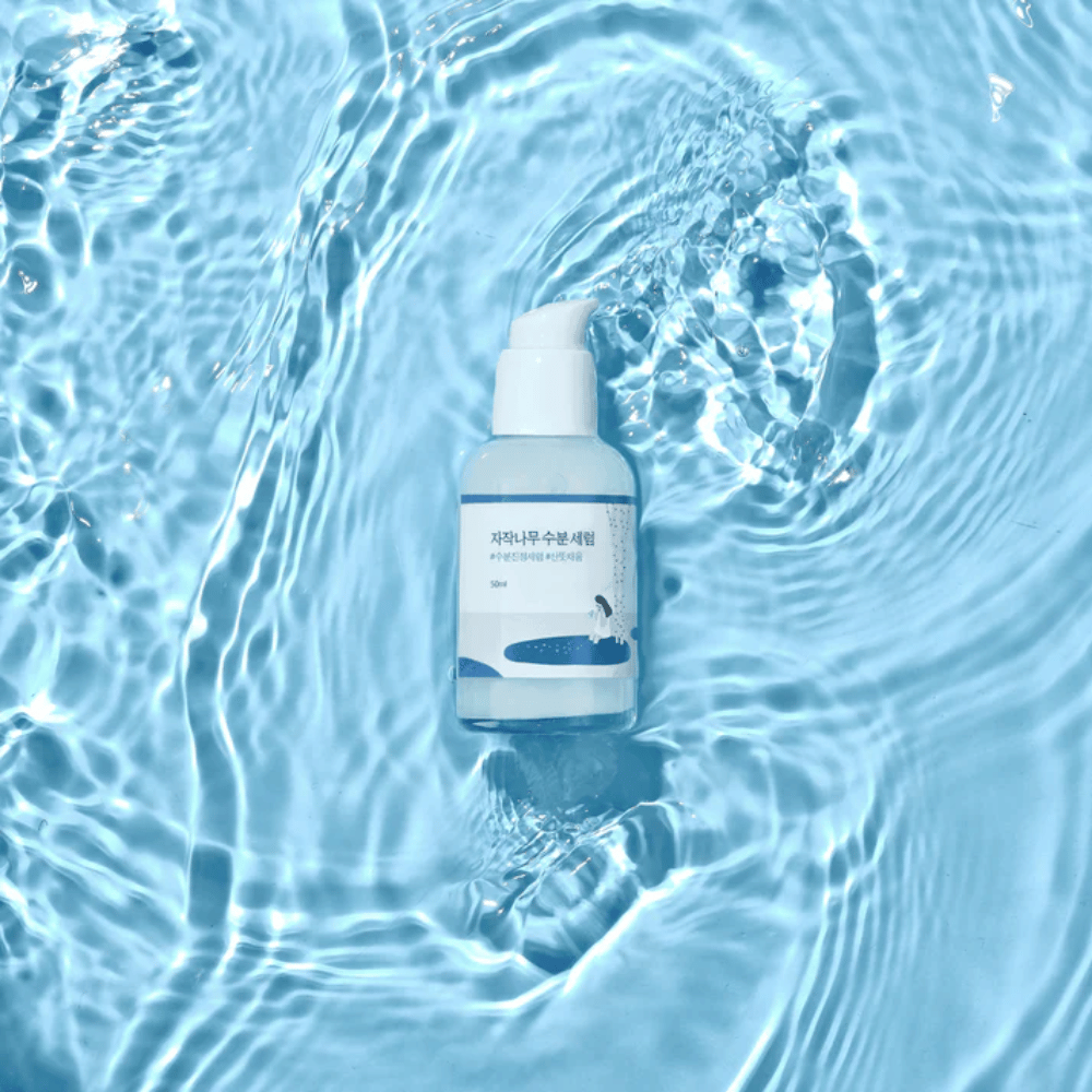 Round Lab Birch Juice Moisturizing Serum w butelce z pompką unoszącej się na niebieskiej wodzie z refleksami słonecznymi.