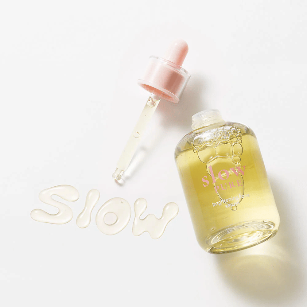 Slow Pure Brightening Tone Serum z otwartą pipetą, tekst napisany w serum na powierzchni: "Slow".