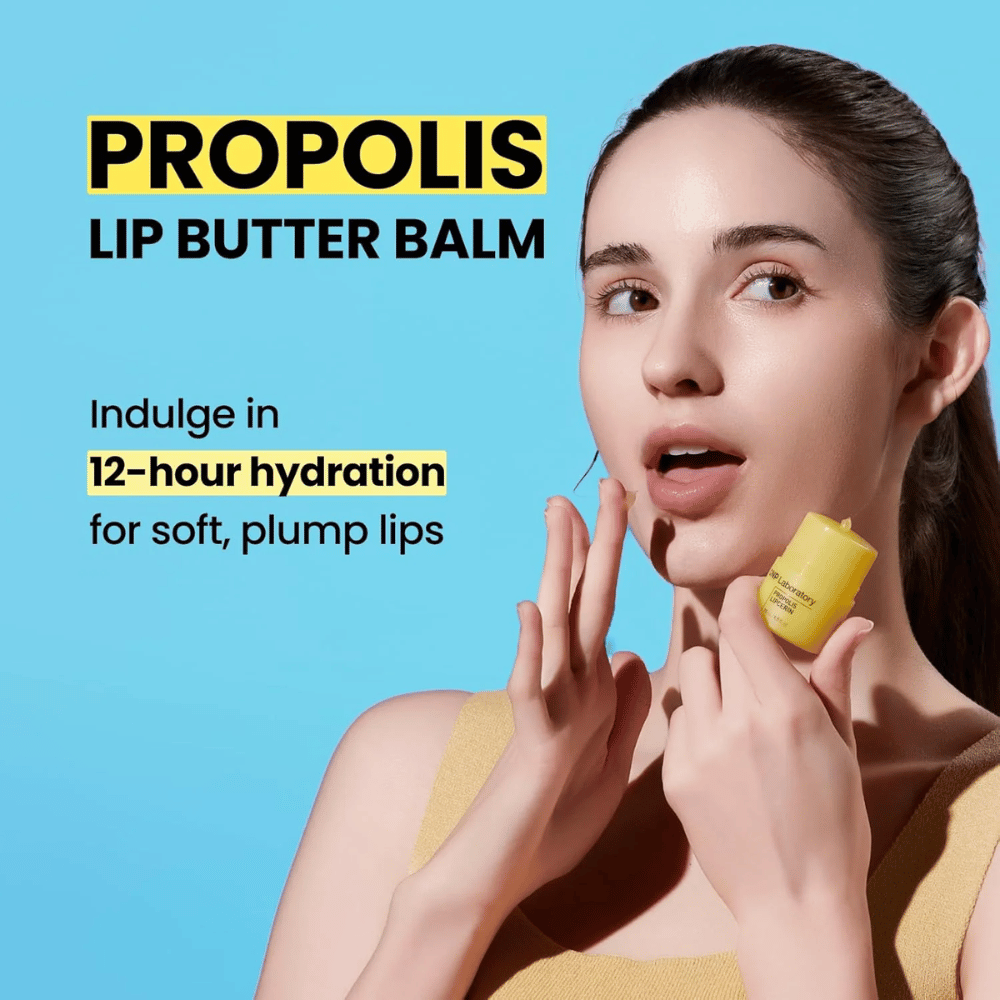 Kobieta aplikuje CNP Laboratory Propolis Lip Butter Balm, wyróżniający się na niebieskim tle. Produkt obiecuje 12 godzin nawilżenia dla miękkich i pełnych ust, co pokazuje żółta tubka, którą trzyma w ręce.