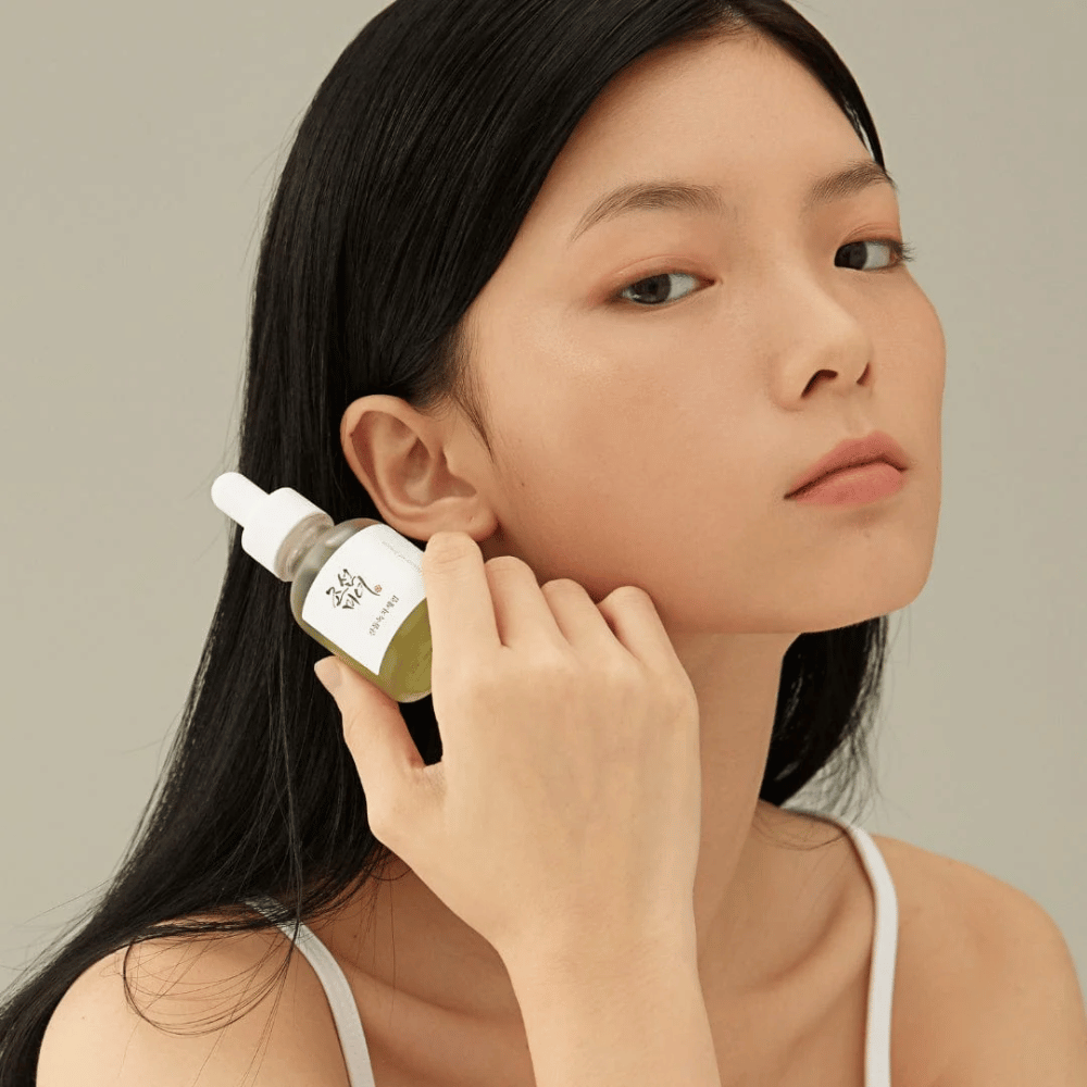 Model trzyma Beauty of Joseon Calming Serum przy policzku – zielona herbata i pantenol wzmacniające barierę skórną.