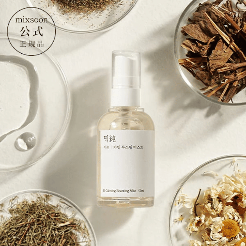 Przezroczysta butelka z rozpylaczem z etykietą 'Calming Boosting Mist' od Mixsoon, otoczona suszonymi ziołami i kwiatami na białych misach na beżowym tle, co podkreśla naturalne składniki produktów.