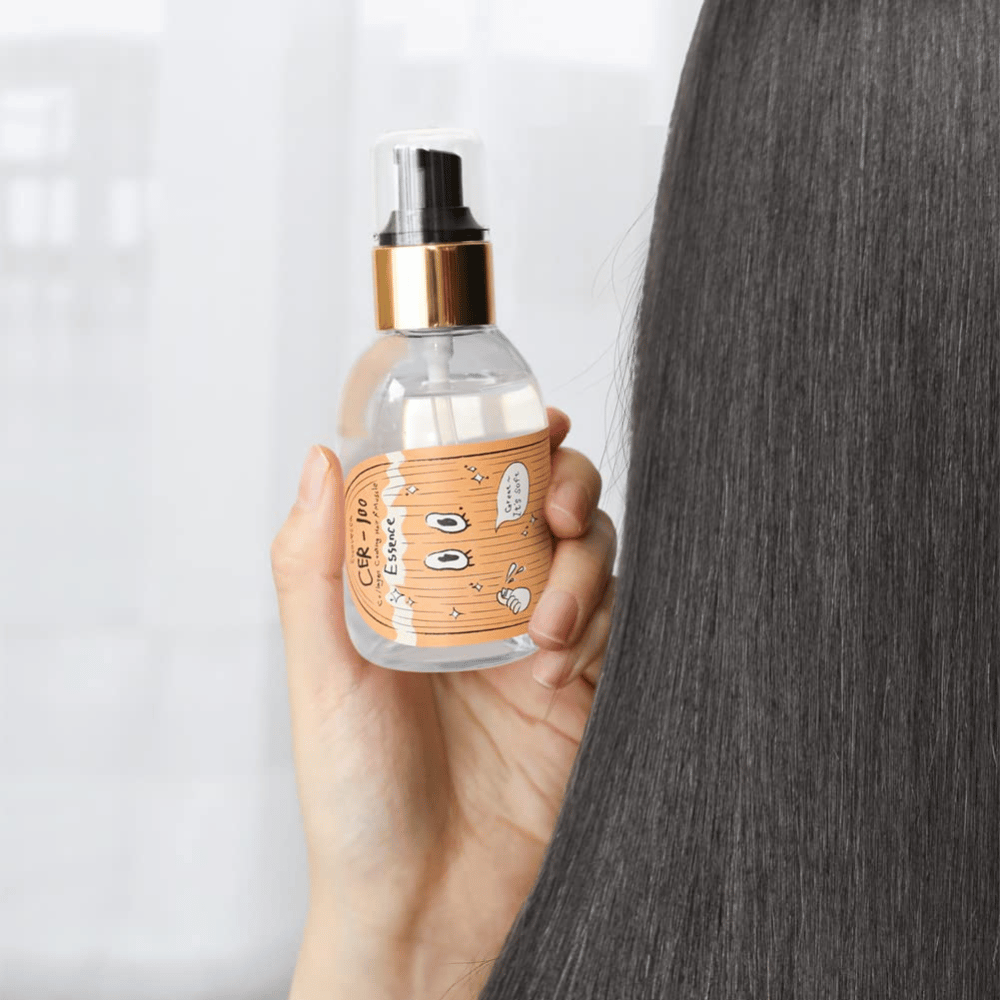 Osoba trzyma CER-100 Hair Essence obok długich, lśniących włosów, aby pokazać miękkość i pielęgnację.