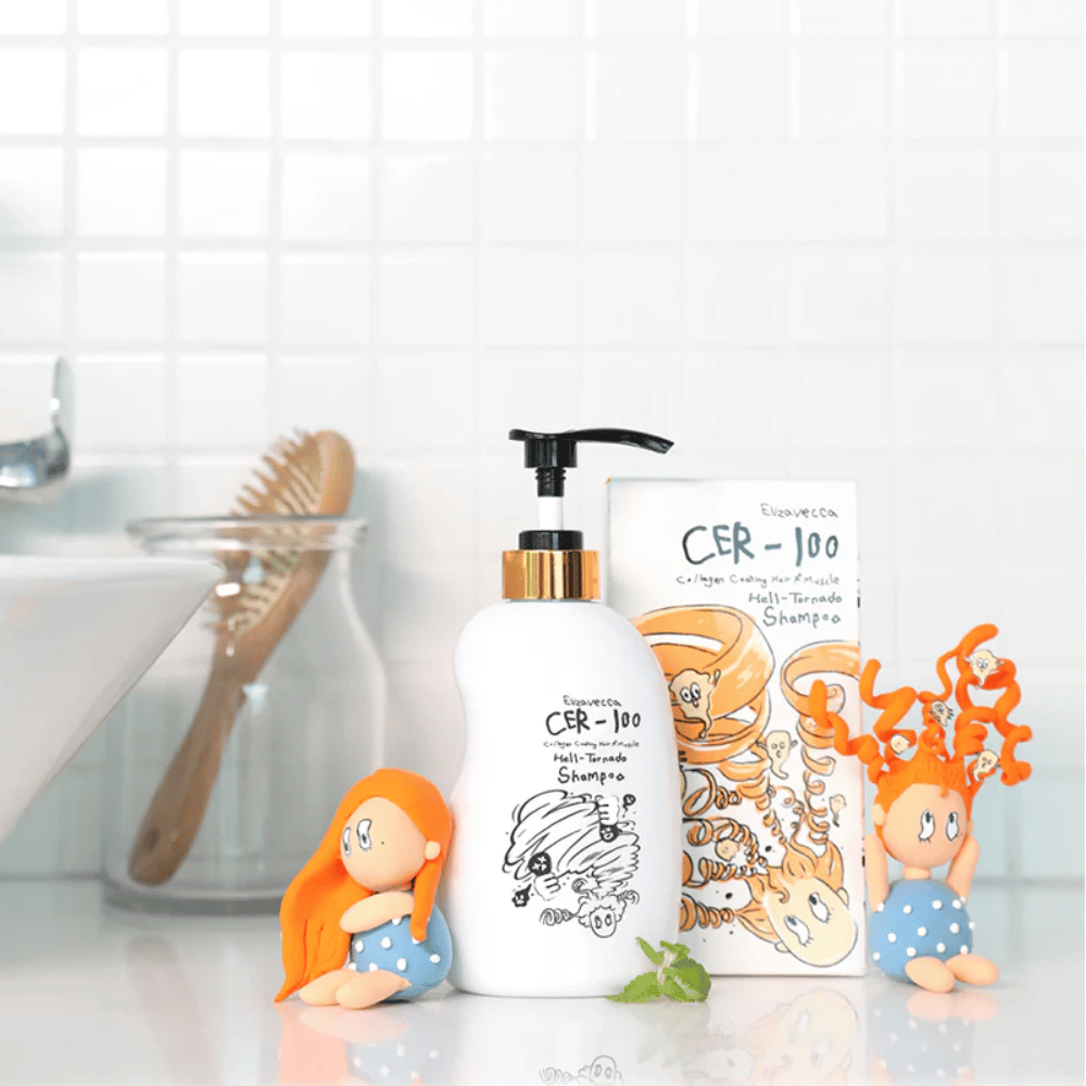 Elizavecca CER-100 Shampoo i kartonik są pokazane w łazienkowym otoczeniu obok szczotki do włosów i dekoracyjnych figurek. Obraz przekazuje codzienną rutynę pielęgnacji włosów oraz użycie produktu w warunkach domowych.