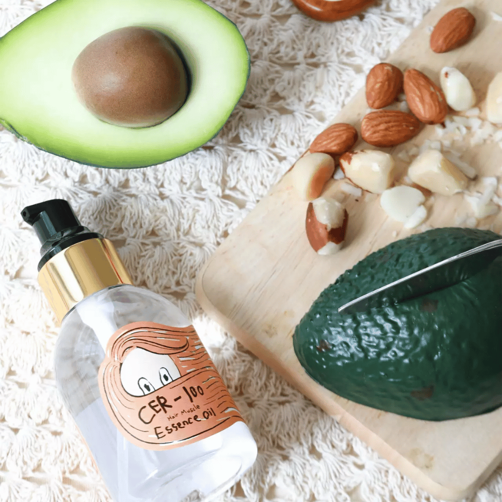 Elizavecca CER-100 Hair Muscle Essence Oil składniki – zbliżenie z awokado i olejami roślinnymi pokazujące odżywczy olejek do włosów, który pomaga zmiękczyć i pielęgnować włosy.