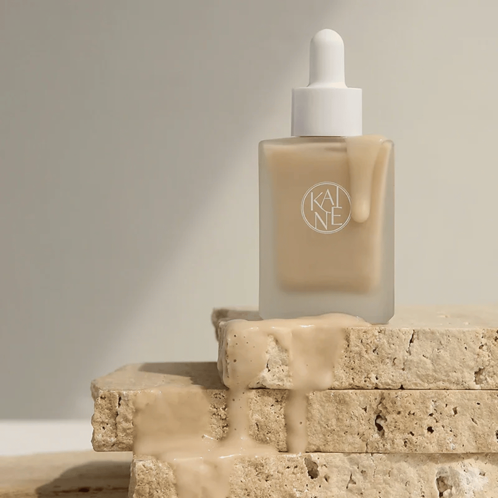 KANE Chaga Collagen Charging Serum w matowej szklanej butelce z pipetą. Kremowa konsystencja spływa po naturalnych kamieniach w miękkim i minimalistycznym świetle.