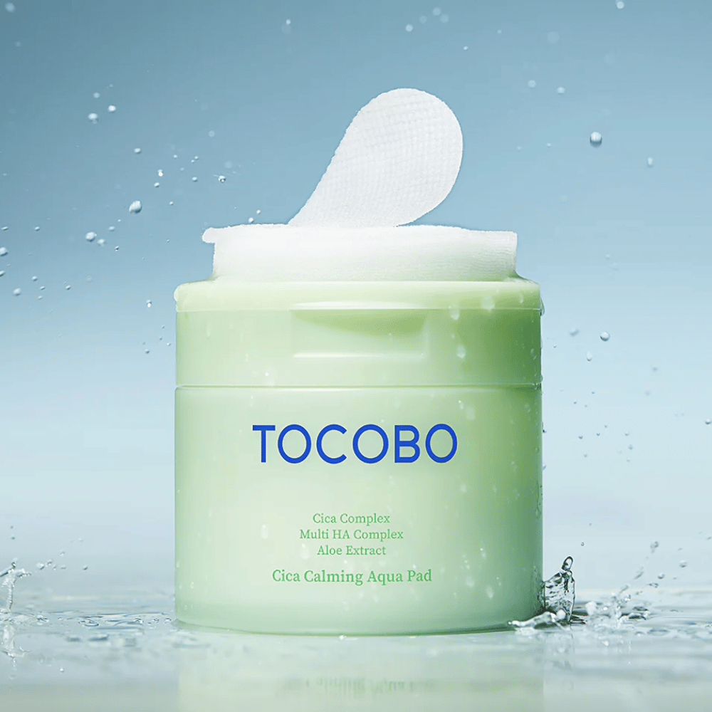 Otwarte opakowanie TOCOBO Cica Calming Aqua Pad, z którego wystaje tonik do twarzy płatek. Krople wody wokół produktu wzmacniają wrażenie intensywnego nawilżenia i świeżości.