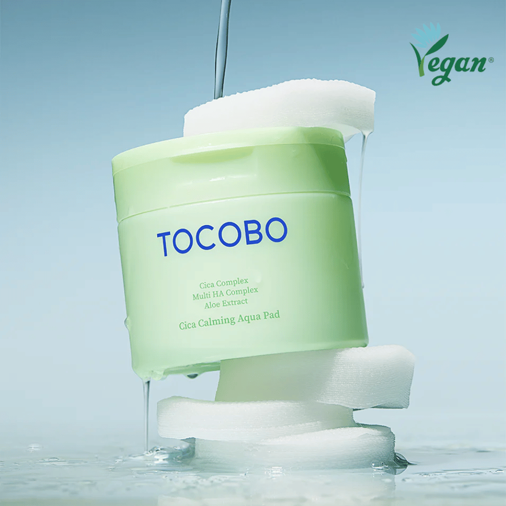 TOCOBO Cica Calming Aqua Pad umieszczony pomiędzy toner pads z płynącą esencją. Symbol wegański podkreśla wegańską formułę produktu i jego przyjazny dla skóry profil.