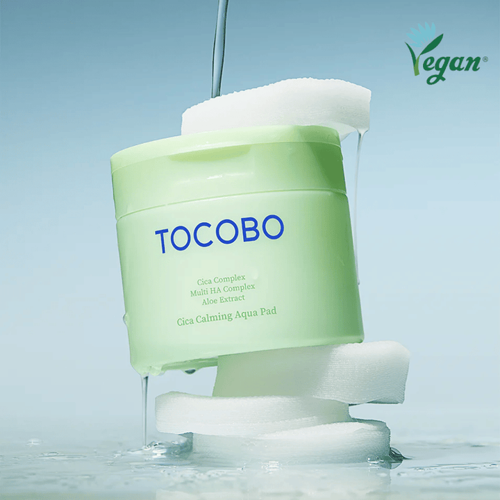 TOCOBO Cica Calming Aqua Pad umieszczony pomiędzy toner pads z płynącą esencją. Symbol wegański podkreśla wegańską formułę produktu i jego przyjazny dla skóry profil.
