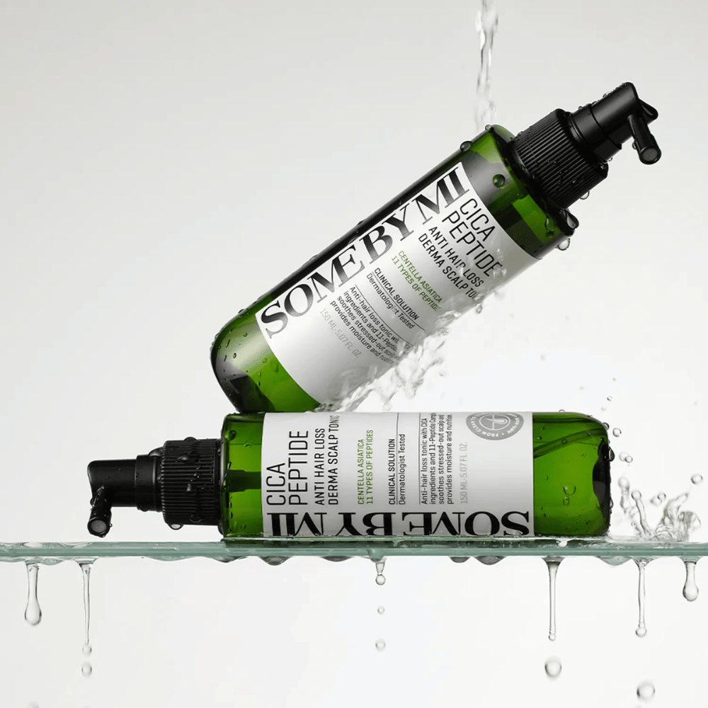 Dwie butelki SOME BY MI Cica Peptide Anti Hair Loss Derma Scalp Tonic leżą w i nad wodą z rozpryskującymi się kroplami, zielone butelki z czarną dyszą natryskową i białą etykietą.
