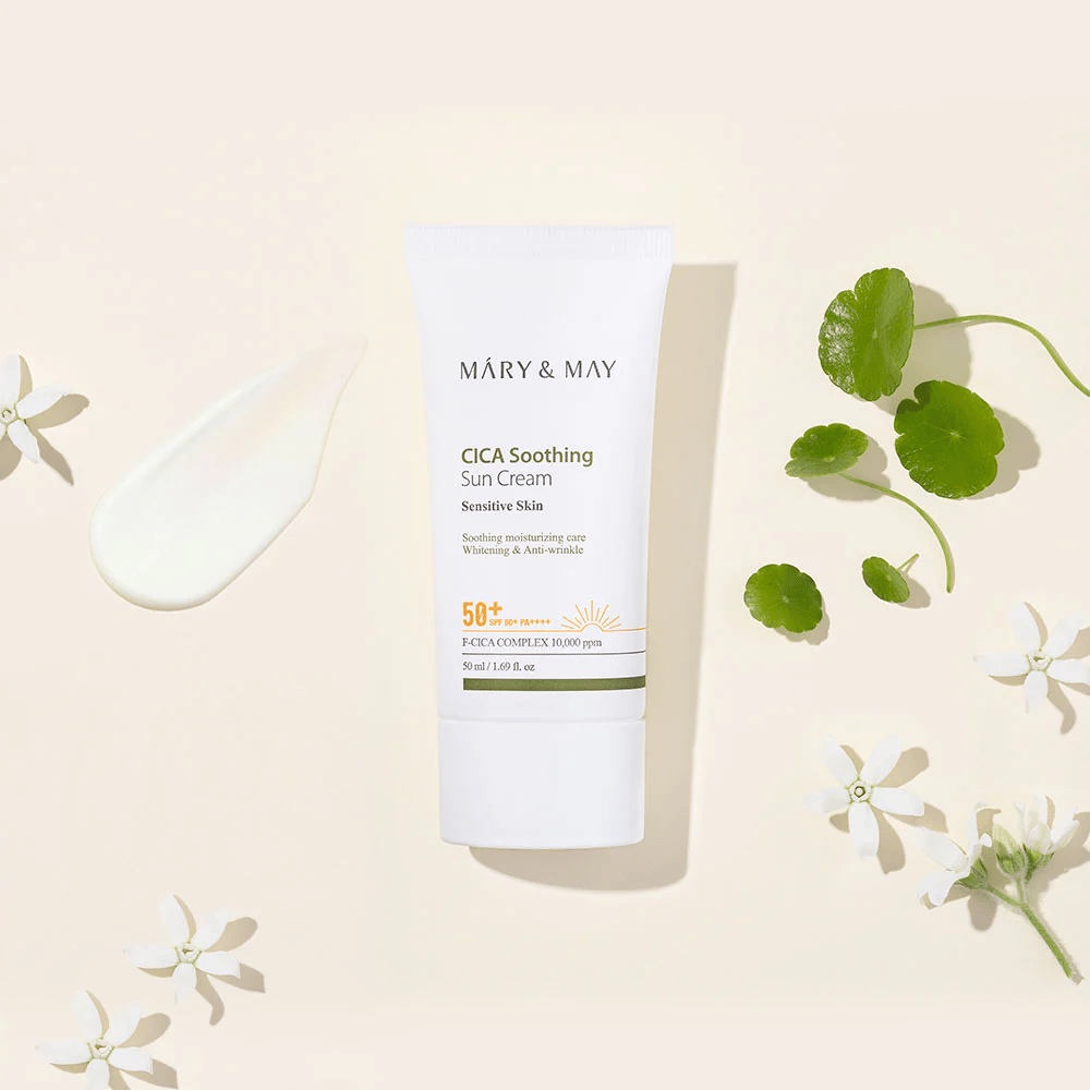 Mary&May CICA Soothing Sun Cream SPF50+ PA++++ przedstawiony wraz z kremową konsystencją, liśćmi centelli i białymi kwiatami. Obraz podkreśla kojące właściwości produktu i jego ukierunkowanie na skórę wrażliwą.
