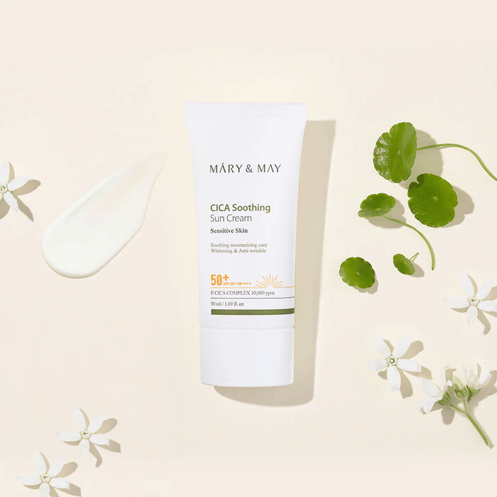 Mary&May CICA Soothing Sun Cream SPF50+ PA++++ przedstawiony wraz z kremową konsystencją, liśćmi centelli i białymi kwiatami. Obraz podkreśla kojące właściwości produktu i jego ukierunkowanie na skórę wrażliwą.