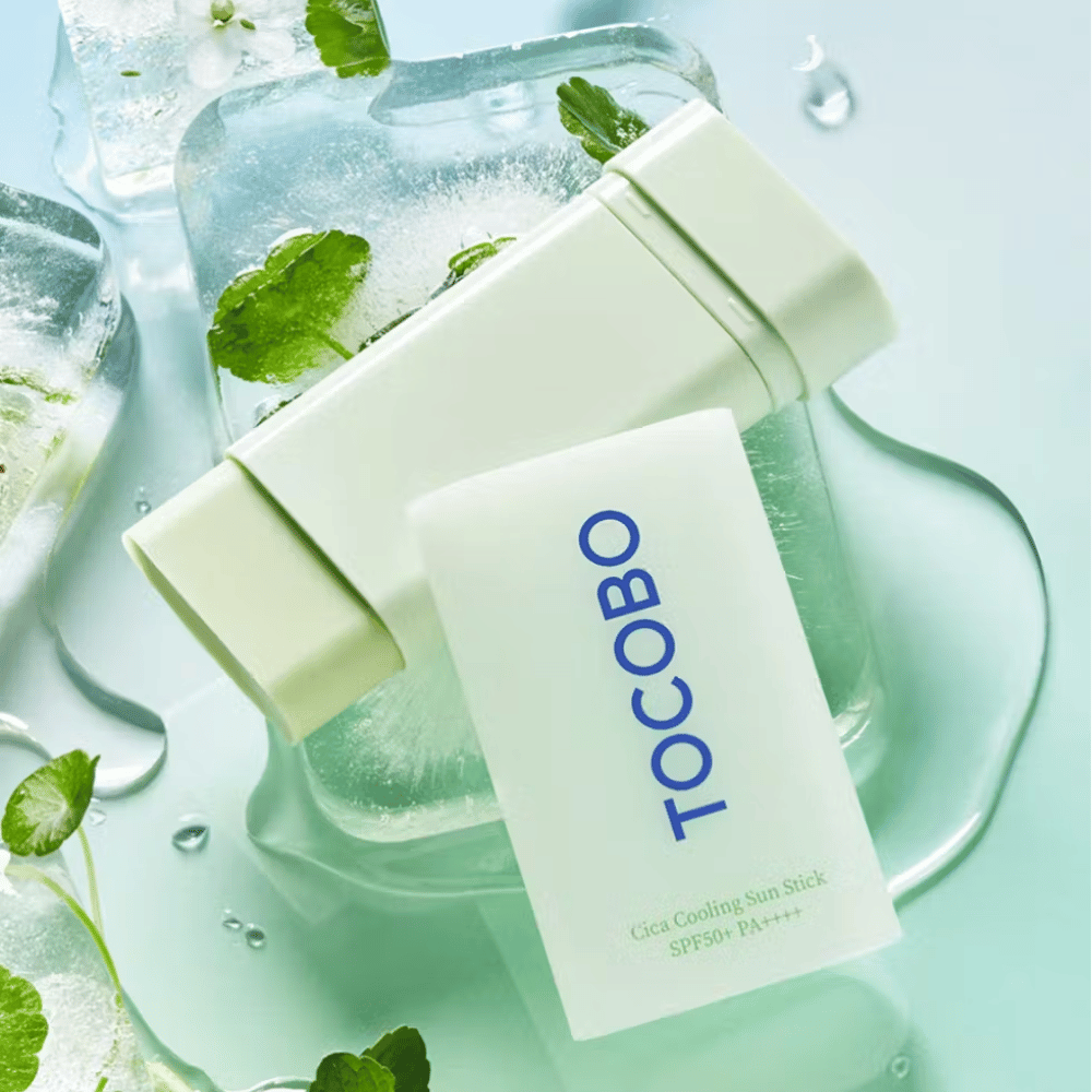 Tocobo Cica Cooling Sun Stick SPF50+ PA++++ na kostkach lodu z zielonymi liśćmi, co przekazuje uczucie chłodzenia i odświeżenia.