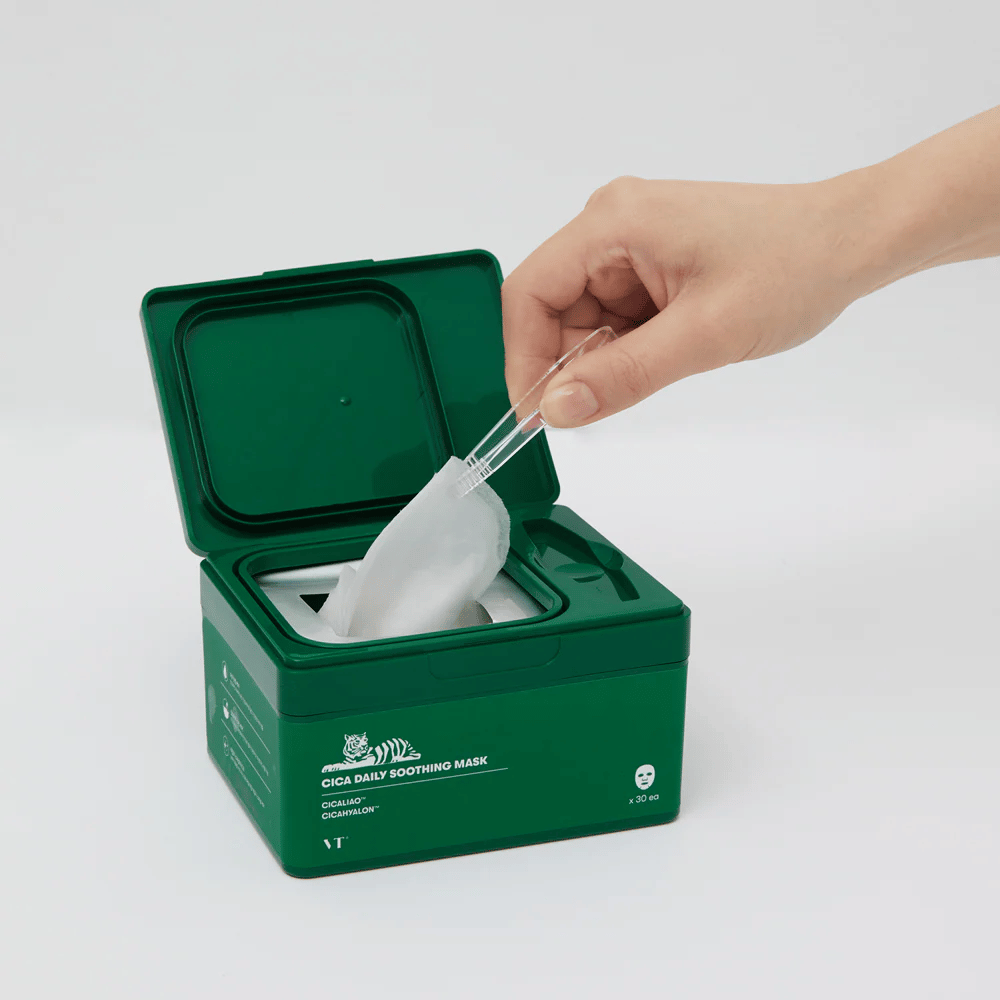Ręka używa pęsety, aby wyjąć Maseczka w płachcie z zielonego pojemnika oznaczonego "Cica Daily Soothing Mask".
