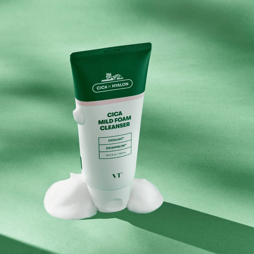 Tuba z VT Cica Mild Foam Cleanser stojąca na zielonym podłożu z pianą wokół podstawy. Produkt ma zielono-biały design i jest reklamowany z CICALIAO™ i CICAHYALON™.