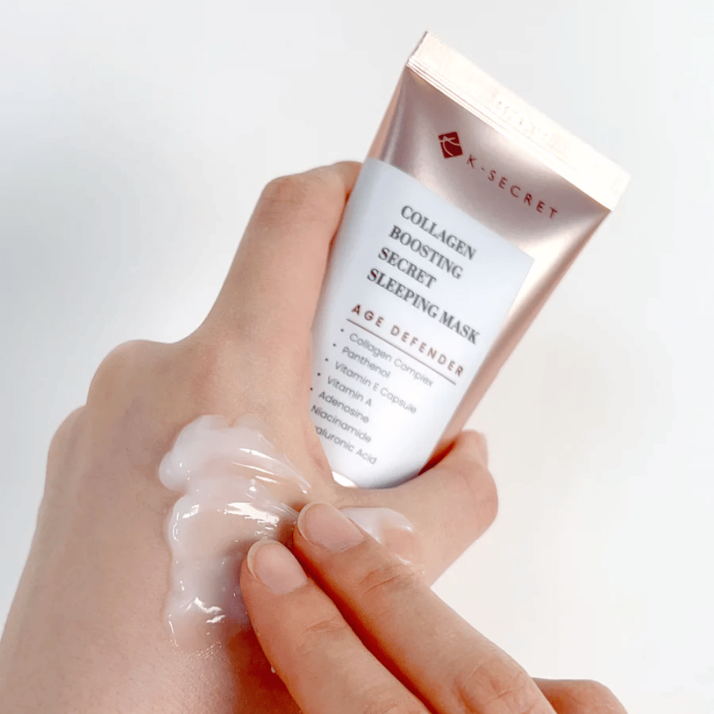 Ręka trzyma Collagen Boosting Secret Sleeping Mask, podczas gdy druga aplikuje hojną ilość kremu na wierzch dłoni – pokazując konsystencję i aplikację produktu.