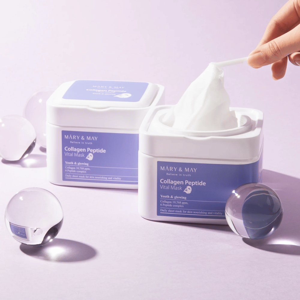 Ręka wyciąga maskę ze słoika MARY & MAY Collagen Peptide Vital Mask. Maska jest przeznaczona do codziennego użytku, aby odżywić skórę i nadać jej blasku, z kolagenem i peptydami wspierającymi młodzieńczość skóry.