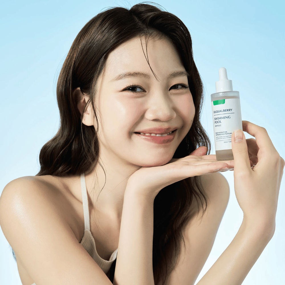 Uśmiechnięta kobieta trzymająca Eqqualberry Swimming Pool Ampoule, nawilżający produkt do pielęgnacji skóry, obiema rękami na jasnoniebieskim tle.