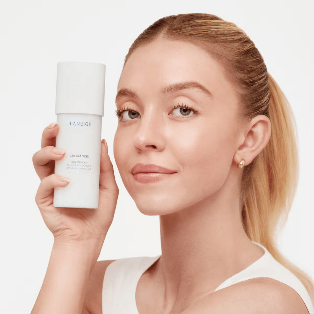 Osoba trzyma Laneige Cream Skin Cerapeptide Refiner w białej butelce. Osoba się uśmiecha i pokazuje produkt, który jest reklamowany jako nawilżający toner i produkt do pielęgnacji skóry.