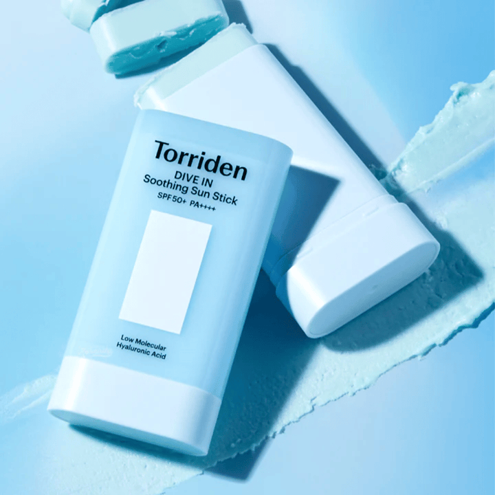 Torriden DIVE IN Soothing Sun Stick SPF50+ PA++++ wraz z rozsmarowaną teksturą produktu, która ilustruje nawilżające działanie i lekką aplikację.